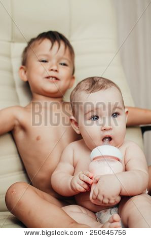 Brother Feeding Little Sister With Milk Or Cereal With A Bottle