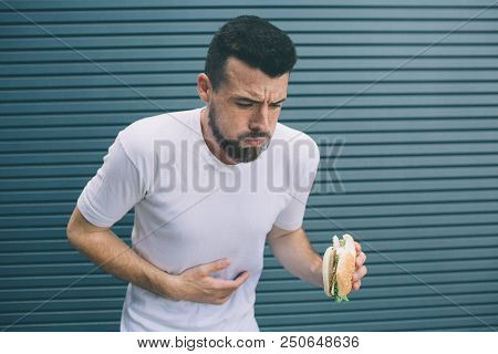 Guy Is Sick. He Is Holding Burger In Hand And Looking Down. Man Is Going To Vomit. Isolated On Strip