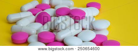 A Pile Of Pills Of White And Pink On A Yellow Background.