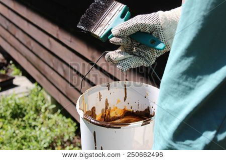 Young Man Painting Ahouse, With Focus On The Paint Brush And Paint Bucket.