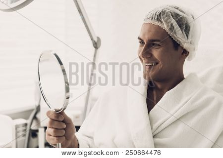 Young Handsome Man In Robe Loking Into Mirror. Smiling Man. Man In White Bathrobe. Anti-aging Cosmet