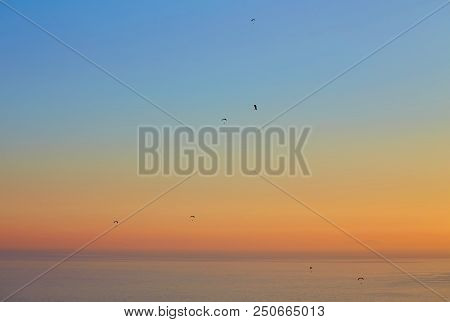 Silhouette Of Powered Paraglider Soaring Flight Over The Sea Against Marvellous Orange Sunset Sky. P