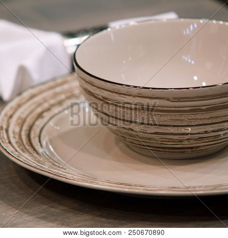 Brown Porcelain Plate, A Bowl And A White Napkin On A Wooden Table