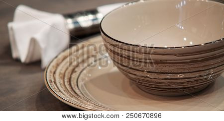 Brown Porcelain Plate, A Bowl And A White Napkin On A Wooden Table