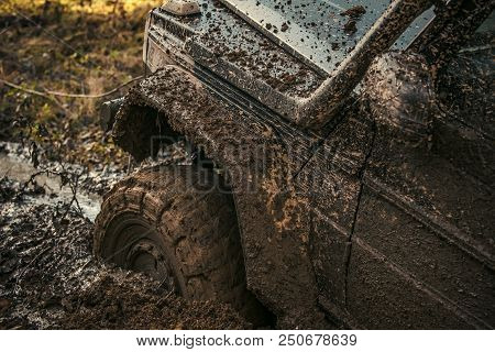 Fragment Of Car Stuck In Dirt, Close Up. Offroad Tire Covered With Mud On Nature Background. Dangero
