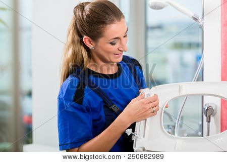 Female maintenance worker checking the quality of a white toilet seat in the showroom of a sanitary ware shop with modern fixtures and accessories 