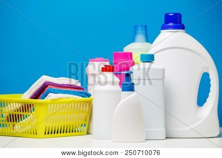 Photo of several bottles of cleaning products and multi-colored towels in basket isolated on blue background