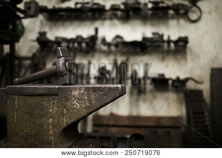 Heavy hammer on iron anvil and set of handtools of blacksmith on background