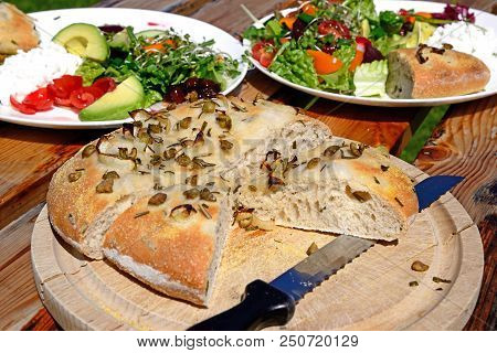 Homemade Italian Rosemary, Green Olive And Onion Focaccia Bread On A Wooden Board With Salad To The 