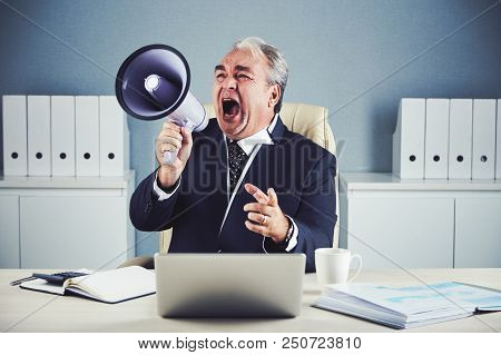 Aged Male In Black Elegant Business Suit Sitting At Office Desk With Gadgets And Documents And Shout