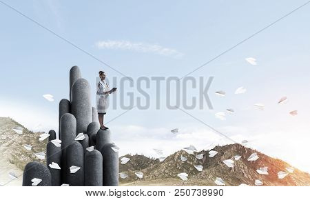 Young Female Doctor With Folder In Hands Satnding On Stone Column