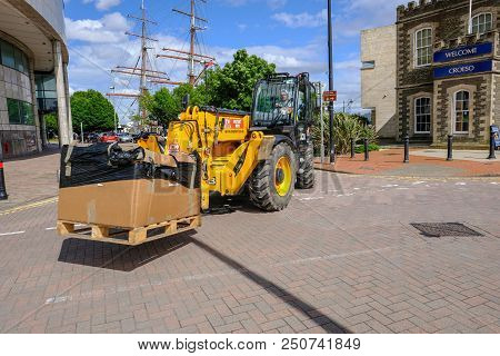Cardiff Bay, Cardiff, Wales - May 20, 2017: Yellow Jcb Vehicle With A Driver, Moving A Large Cardboa