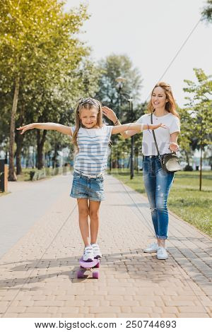 First Time. Blonde-haired Smiling Active Girl Feeling Happy Having Her First Time On Skateboard Near