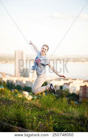 Portrait Of A Woman In An American T-shirt On A Background Of Saratov, Russia, Jumping Up. View Of T