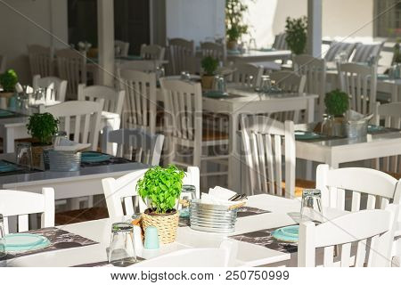 Mediterranean Outdoor Restaurant With White Tables And Bazil Pots In Sunlight