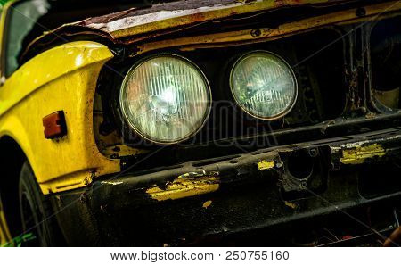 Old Wrecked Car In Vintage Style. Abandoned Rusty Yellow Car In The Forest. Closeup Front View Headl