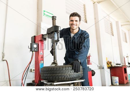 Portrait Of Smiling Mid Adult Serviceman In Uniform Using Tire Changer At Garage