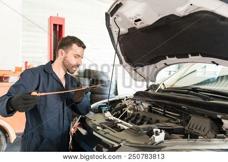 Mid Adult Male Engineer Checking Oil Level In Car Engine During Routine Maintenance At Workshop