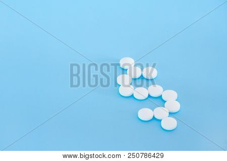 White Pills Spilling Forming A Dollar Sign On A Blue Background.