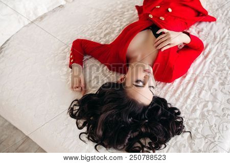Above View Of Goergous And Fashionable Woman In Red Low Neckline Dress Lying And Resting On White Be