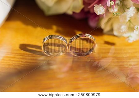 Beautiful Toned Picture With Wedding Rings Lie On A Wooden Surface Against The Background Of A Bouqu