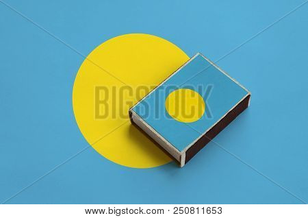 Palau Flag  Is Pictured On A Matchbox That Lies On A Large Flag.