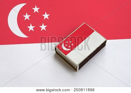 Singapore Flag  Is Pictured On A Matchbox That Lies On A Large Flag.