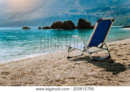 Beach Chair From Back On Tranquil Pebble Beach. Amazing View To Impressive Rocks In The Water. Seren