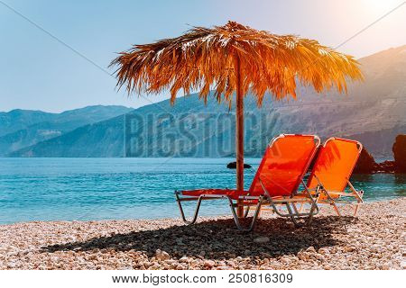 Lovely Isolated Beach And Sunbeds Under Straw Umbrella At Warm Sunset Light.