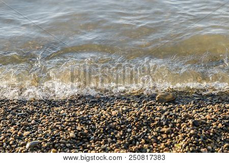Pebbles On The Beach Pebbles On The Sea Shore And Waves Of Water Illuminated By The Rays Of The Sun