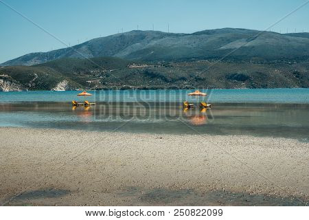 Sunlougers Below Umbrellas In The Shallow Water Of Turquoise Bay. Opposite Mountainous Island With W
