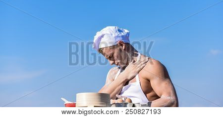 Baker Concept. Man On Busy Face Wears Cooking Hat And Apron, Sky On Background. Chef Cook Preparing 