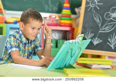 Young Boy Doing Homework And Pointing Up With Finger In Classroom
