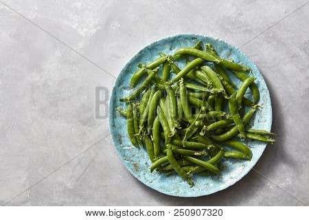 Natural organic green peas in sticks on a blue ceramic plate on a gray marble kitchen table. Top view.