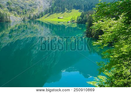 Mirror Lake Obersee Surrounded By Young Greenery. Alpine Meadow And Rural Hut.
