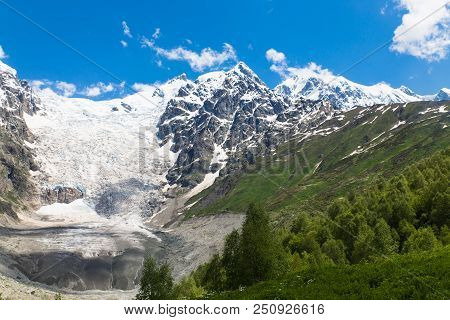 Adishi Glacier With Blue Sky On Background And Green Trees On Foreground In Georgia, Svaneti Region 