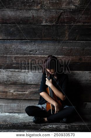The Lady Is Sitting On Grunge Surface Cement Floor,hold Violin And Bow In Her Arms,turn Face Down To