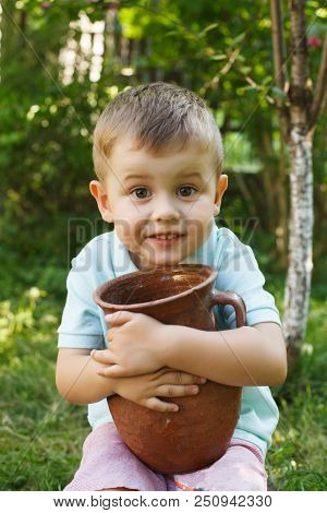 Cute Little Boy Holding A Old Clay Pot. Milk Jug.