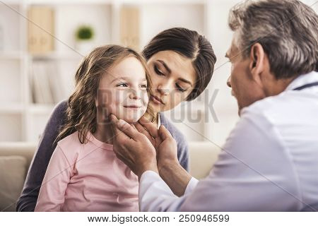Careful Doctor Examining Small Child. Woman Looking At Smiling Little Girl. Doctor Calms Small Patie