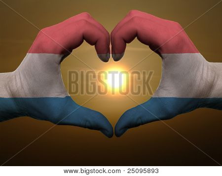 Coração e amor gesto por mãos coloridas na bandeira da Holanda durante o belo nascer do sol