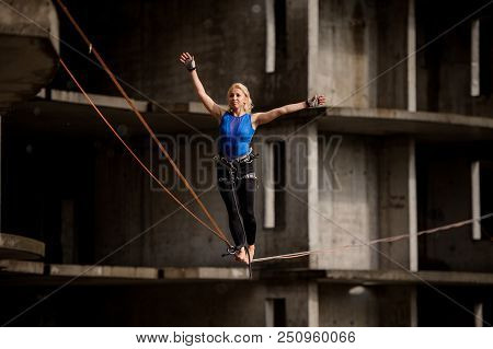 Female Equilibrist Balancing With Arms Raised On The Slackline Rope On The Background Of Section Of 