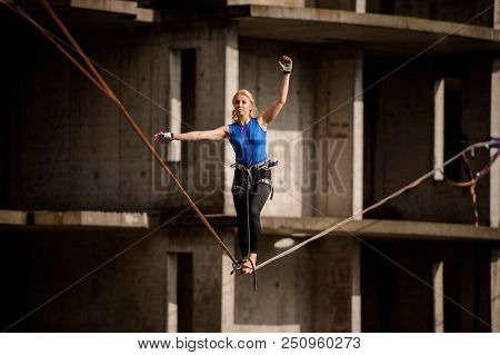 Female Equilibrist Standing With One Arm Raised And Other To The Left On The Slackline On The Backgr