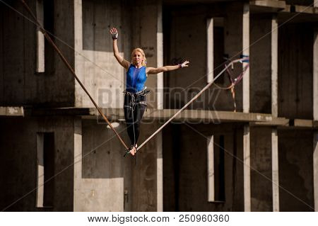 Female Equilibrist Balancing With One Arm Raised And Other To The Right On The Slackline On The Back