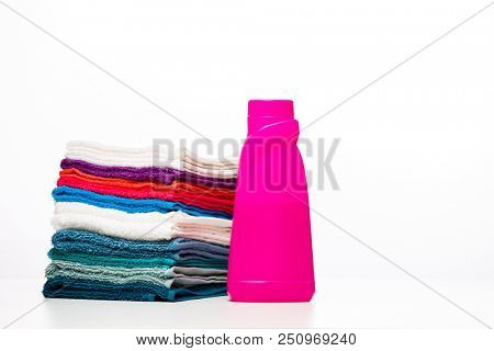 Photo of one pink bottle of detergent and multi-colored towels on clean white background