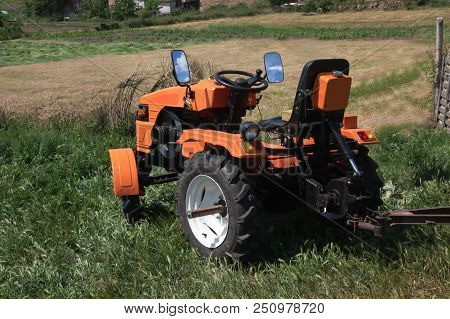 The Orange Minitractor Works In The Field. Agricultural Multifunction Machine With A Trailer Collect