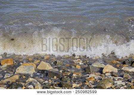 Pebbles On The Beach Pebbles On The Sea Shore And Waves Of Water Illuminated By The Rays Of The Sun