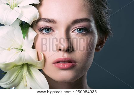 Close-up Portrait Of Attractive Young Woman Surrounded With White Lilium Flowers Isolated On Grey