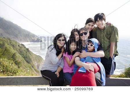 Famiglia multirazziale di sette seduto dall'Oceano Pacifico. Little Boy è disabilitato con paralisi cerebrale