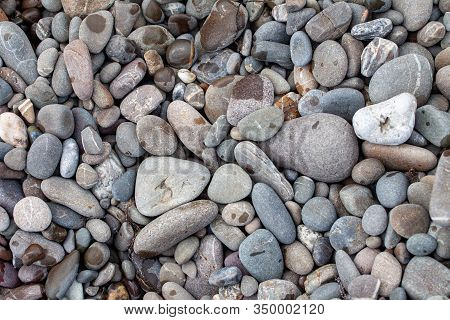 Sea Pebbles Colored Granite On The Beach Background Stones. The Shore Of The Beach With Sand And Peb