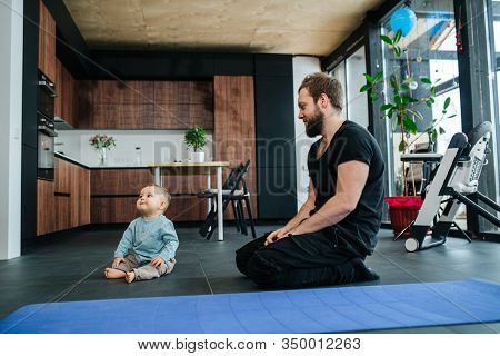 Father Sitting On His Legs, Looking At His Infant Baby Next To Him